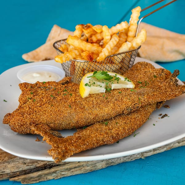 Crispy fried catfish fillets with crinkle-cut fries, tartar sauce, and a lemon wedge.
