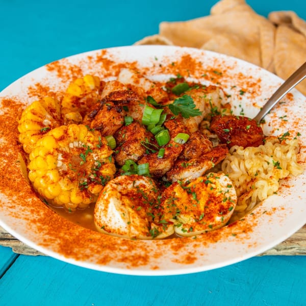 Catfish Willy's seafood boil with shrimp, corn, eggs, sausage, and noodles, generously seasoned with paprika.