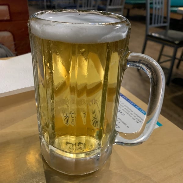 A frosty mug of golden beer with a foamy head sits on a table at Catfish Willy's.