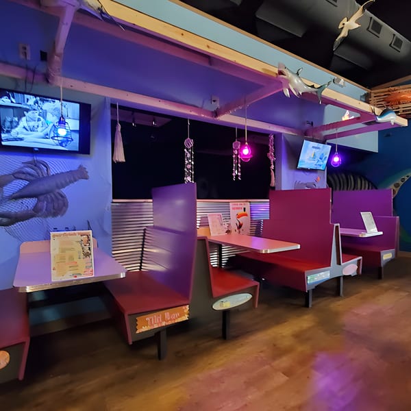 Interior of Catfish Willy's, featuring purple and red booths, TVs, and seafood-themed decor under blue lighting.