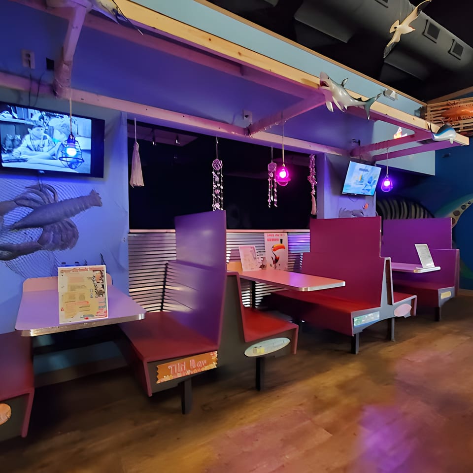 Interior of Catfish Willy's, featuring purple and red booths, TVs, and seafood-themed decor under blue lighting.