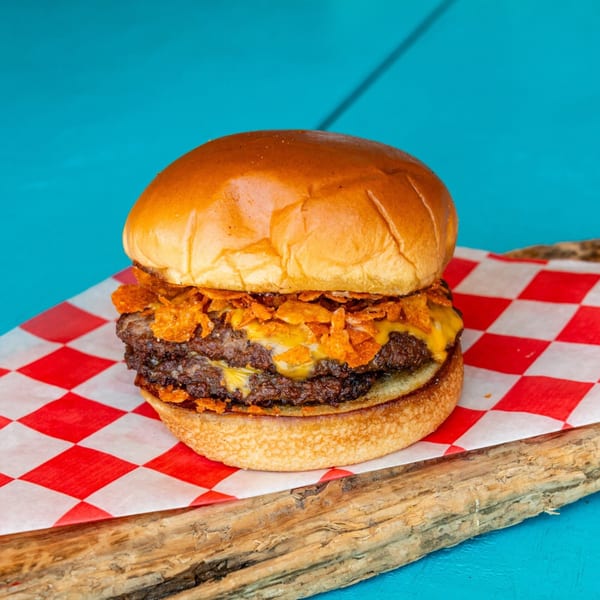 Double cheeseburger topped with crunchy chips on a red and white checkered paper.