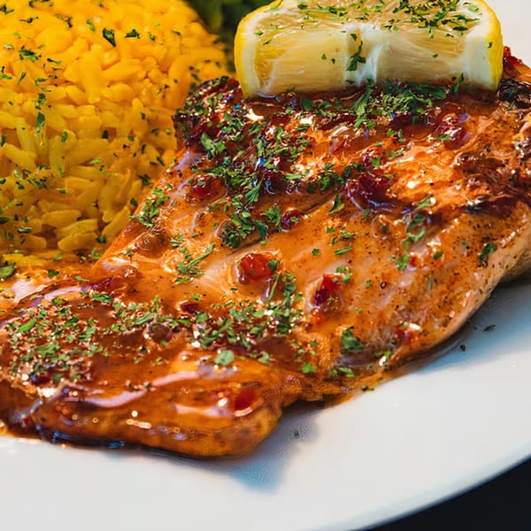 Catfish Willy's grilled salmon with lemon, parsley, and yellow rice on a white plate.