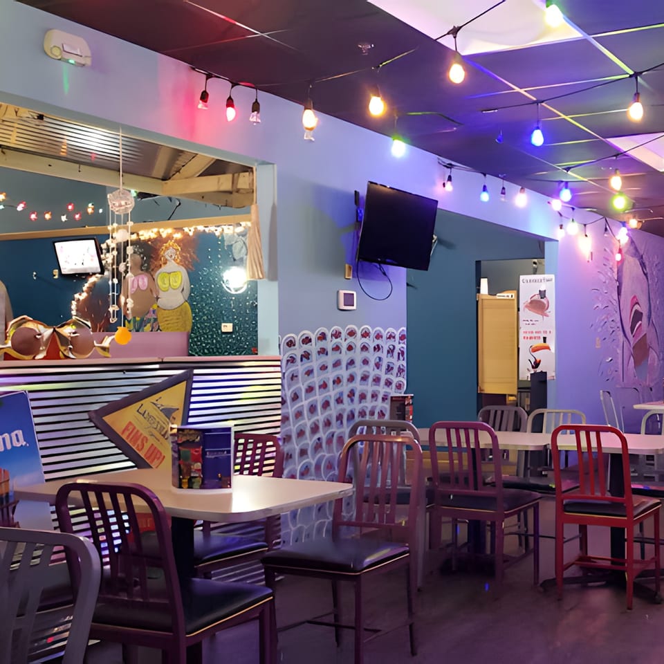 Interior of Catfish Willy's, featuring colorful string lights, tables, chairs, and mermaid decor.