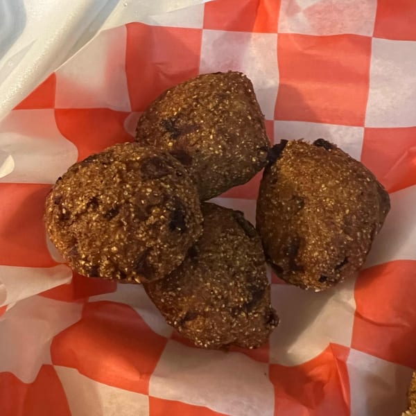Four dark brown hushpuppies with a speckled texture, served in a red and white checkered paper.