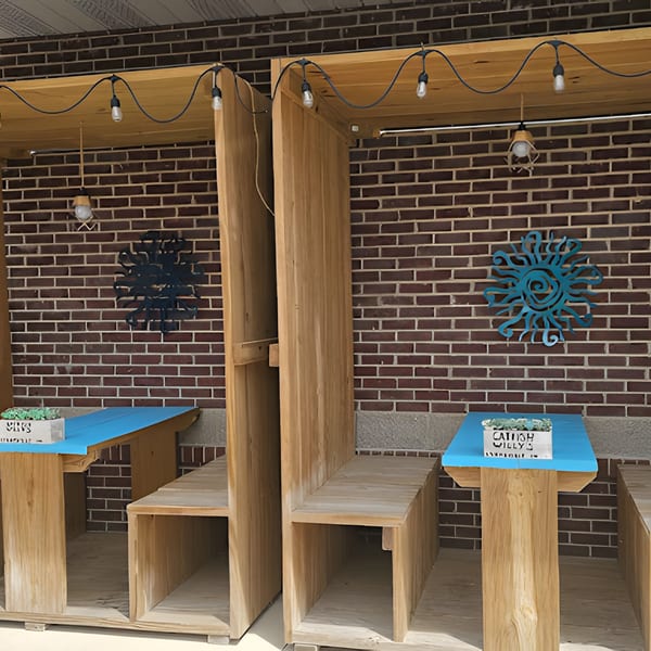Outdoor seating area at Catfish Willy's with wooden booths, blue tables, string lights, and brick wall decor.